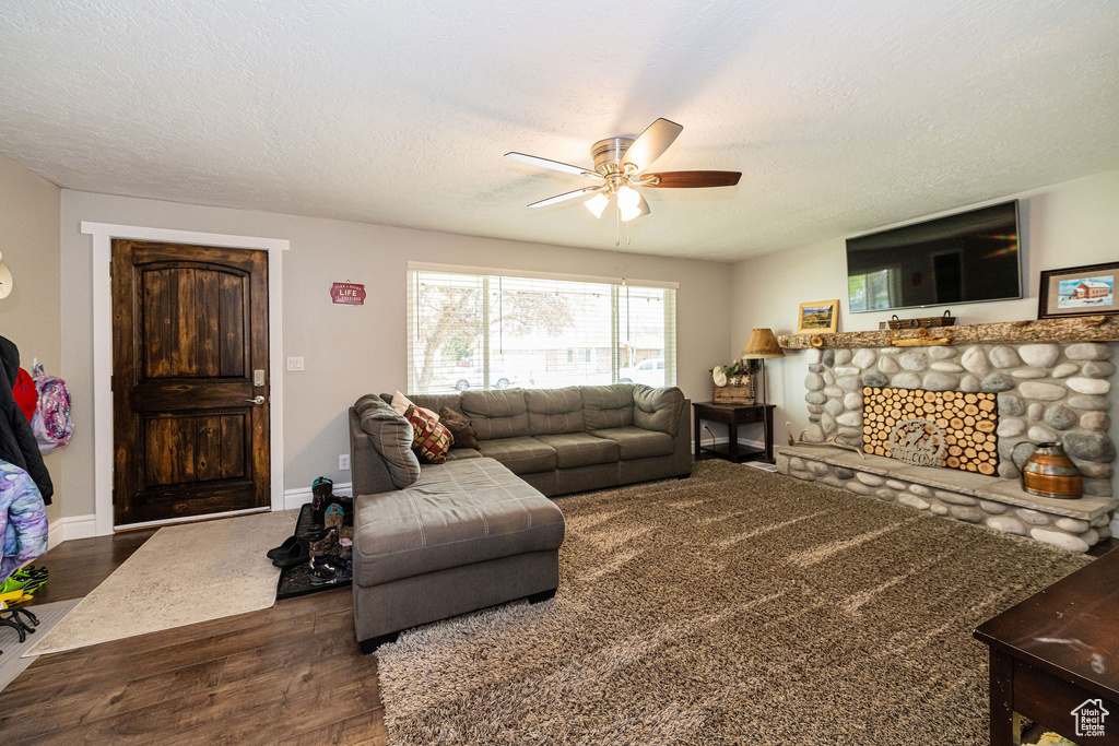 Living area with ceiling fan, a textured ceiling, a stone fireplace, wood finished floors, and baseboards