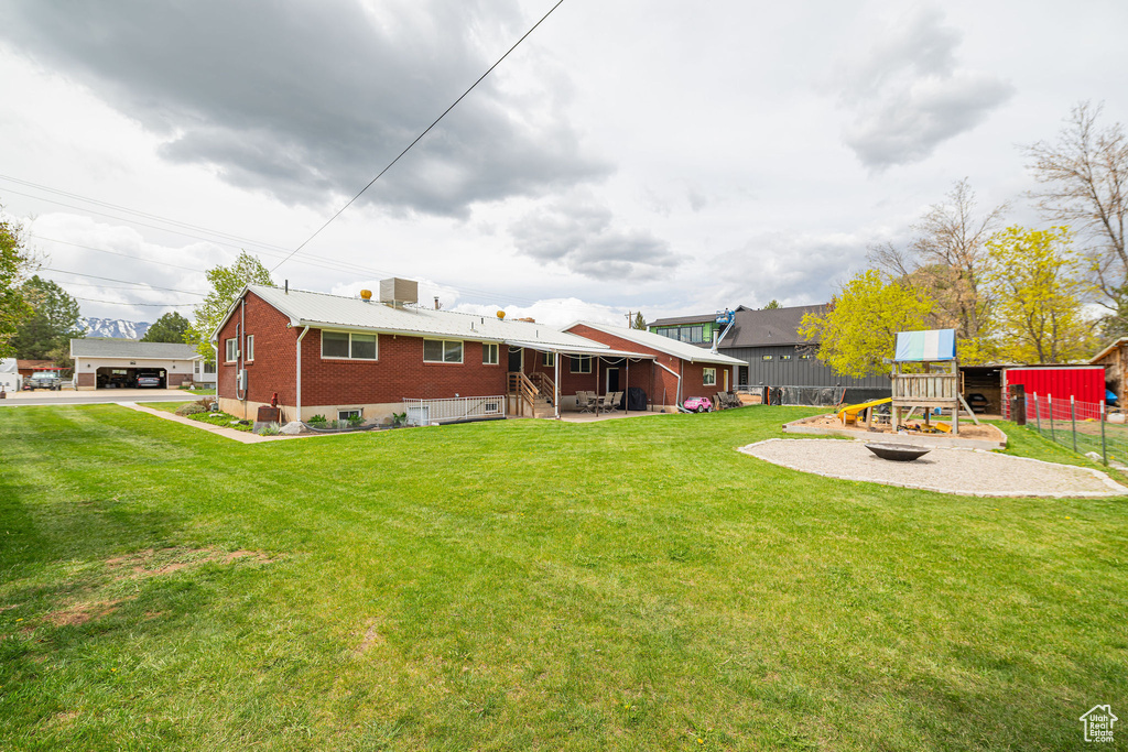 Back of property with a playground, fence, a yard, and brick siding