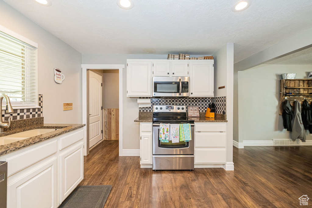 Kitchen with decorative backsplash, appliances with stainless steel finishes, stone counters, and a sink