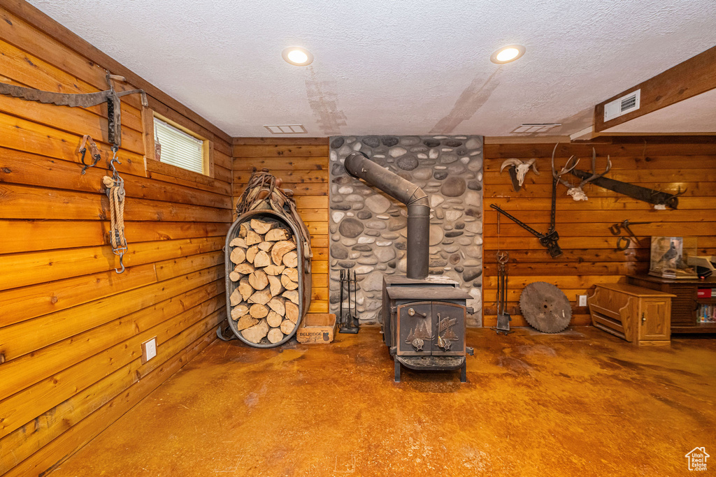 Interior space with finished concrete floors, a wood stove, a textured ceiling, and wood walls