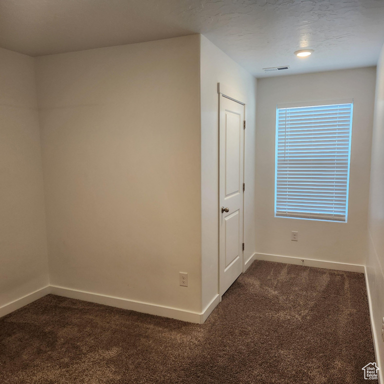 Empty room featuring baseboards, visible vents, and dark carpet