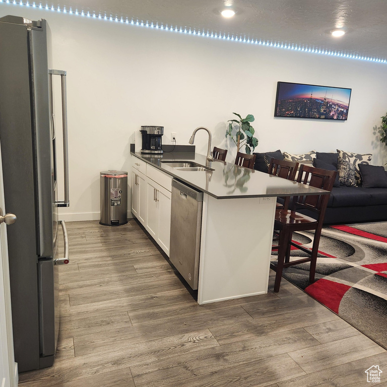 Kitchen with appliances with stainless steel finishes, wood finished floors, a sink, a peninsula, and white cabinetry