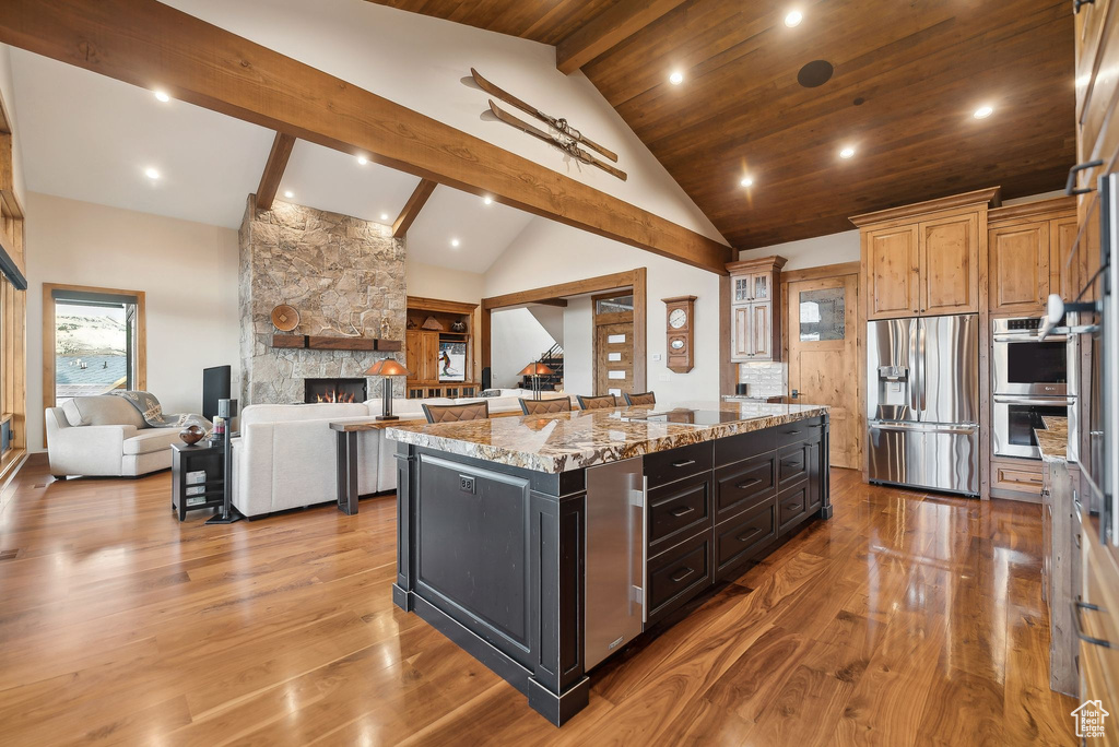 Kitchen featuring appliances with stainless steel finishes, a kitchen island, light wood-type flooring, light stone countertops, and a fireplace