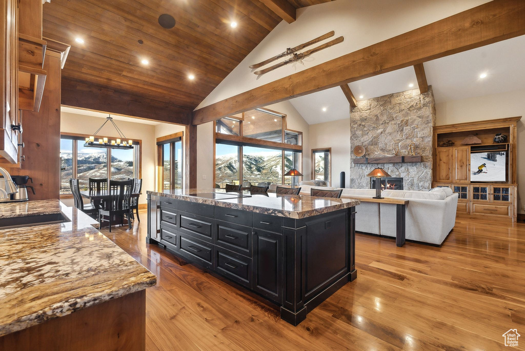 Kitchen featuring a sink, beam ceiling, dark cabinetry, wood finished floors, and ceiling fan with notable chandelier