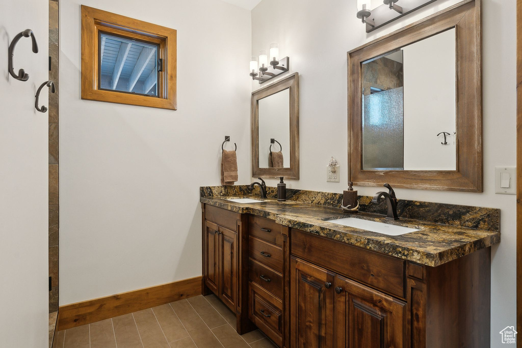 Full bathroom featuring a tile shower, double vanity, a sink, and baseboards