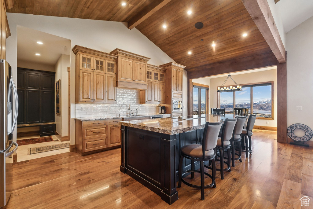 Kitchen with vaulted ceiling with beams, a center island, light wood-style flooring, and appliances with stainless steel finishes