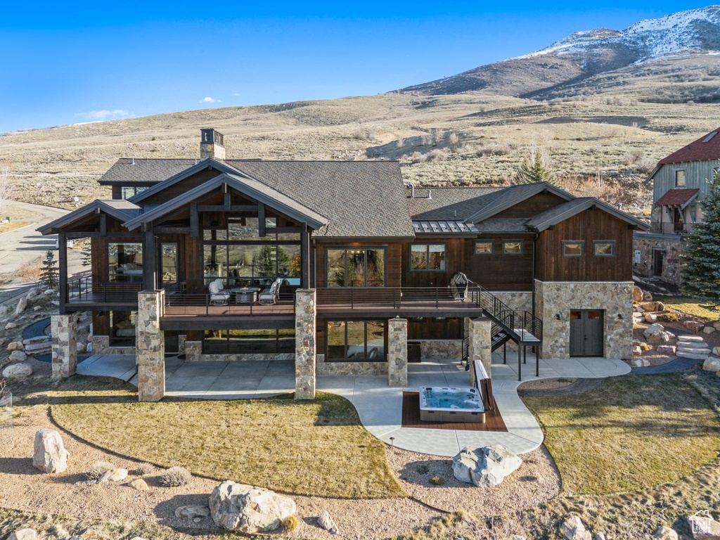 Back of house featuring stone siding, a deck with mountain view, and a patio area