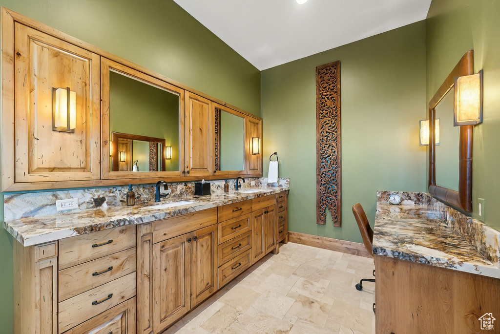 Full bath with tasteful backsplash, a sink, double vanity, stone finish flooring, and baseboards