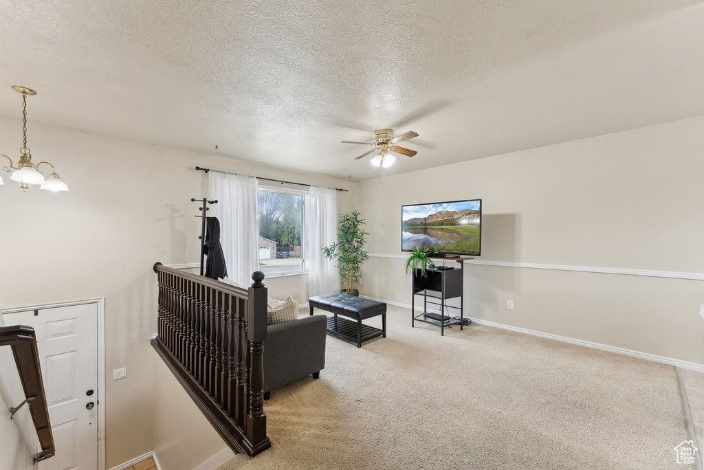Living room featuring carpet floors, a textured ceiling, ceiling fan with notable chandelier, and baseboards