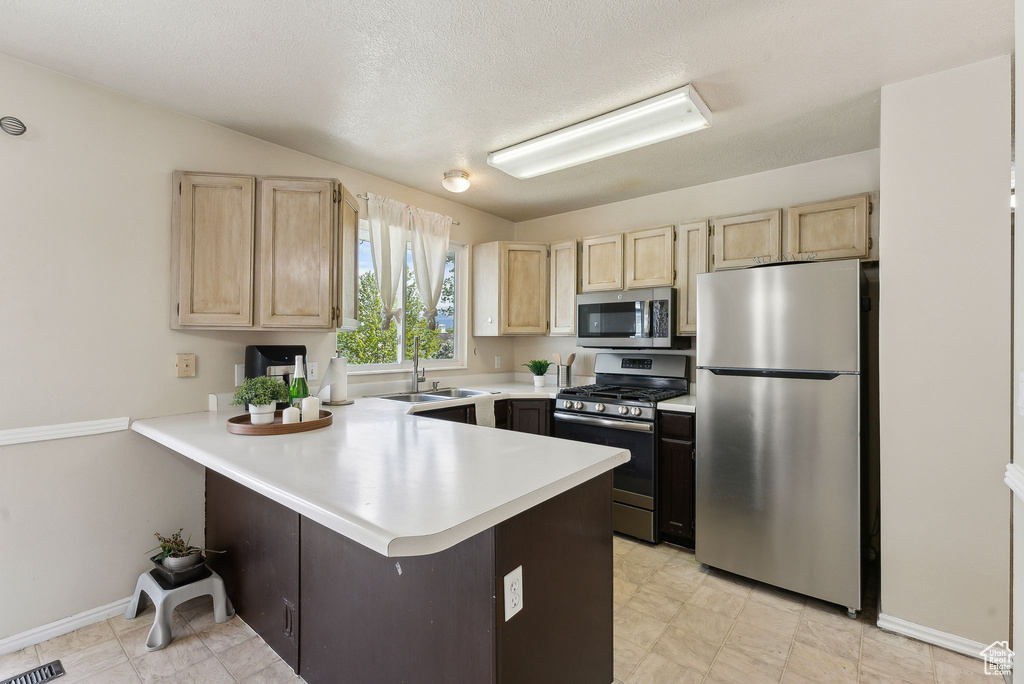 Kitchen featuring a peninsula, light brown cabinetry, light countertops, a sink, and appliances with stainless steel finishes