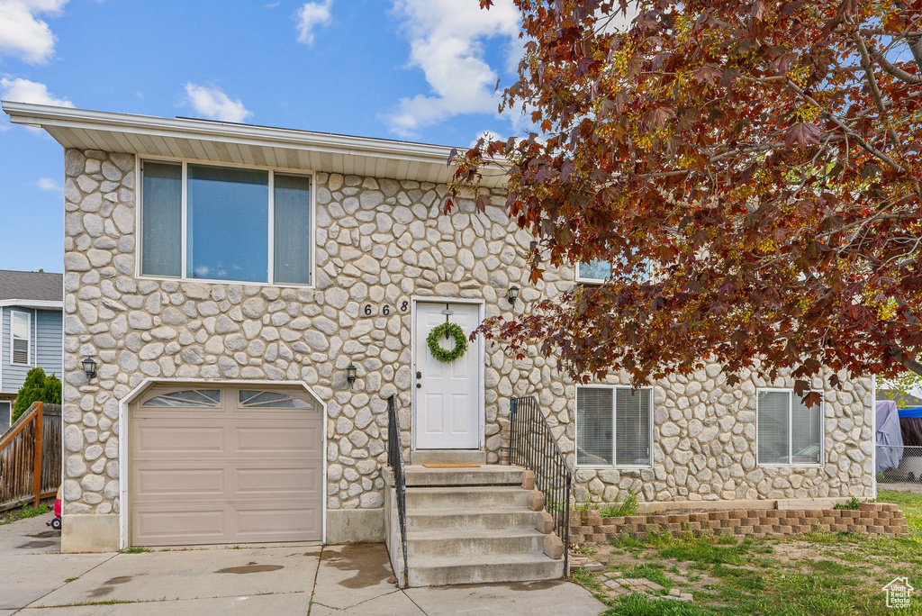 View of front of property featuring entry steps, driveway, stone siding, and a garage