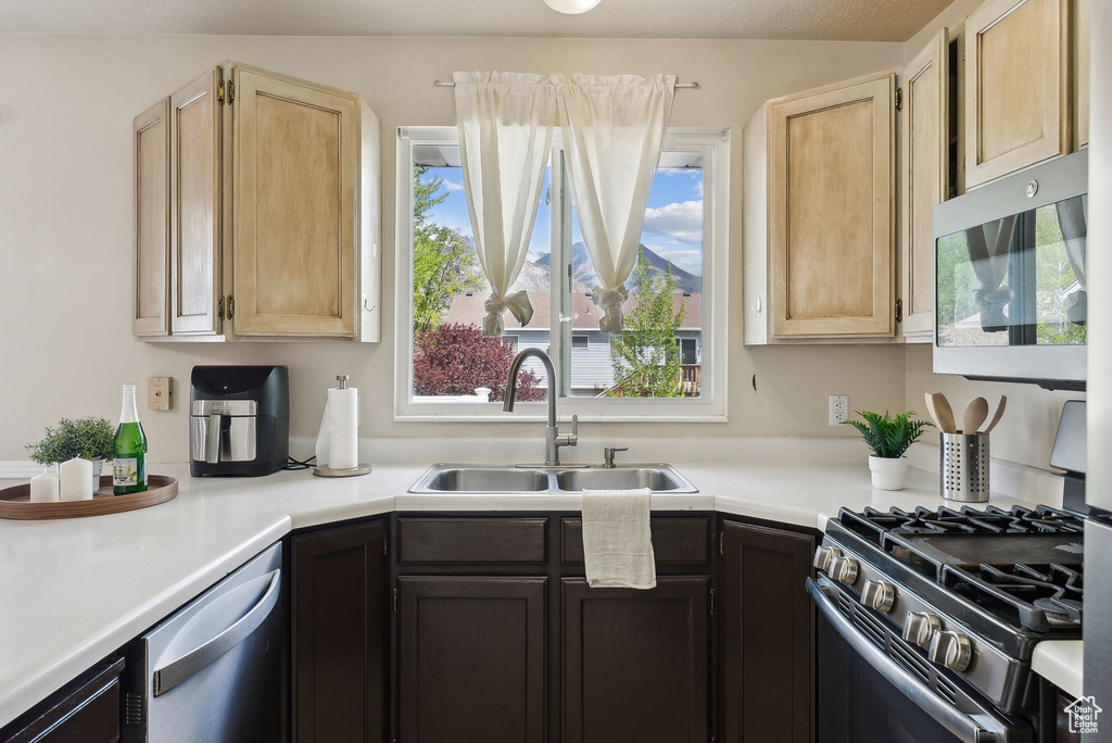 Kitchen with light brown cabinetry, stainless steel appliances, a sink, and light countertops
