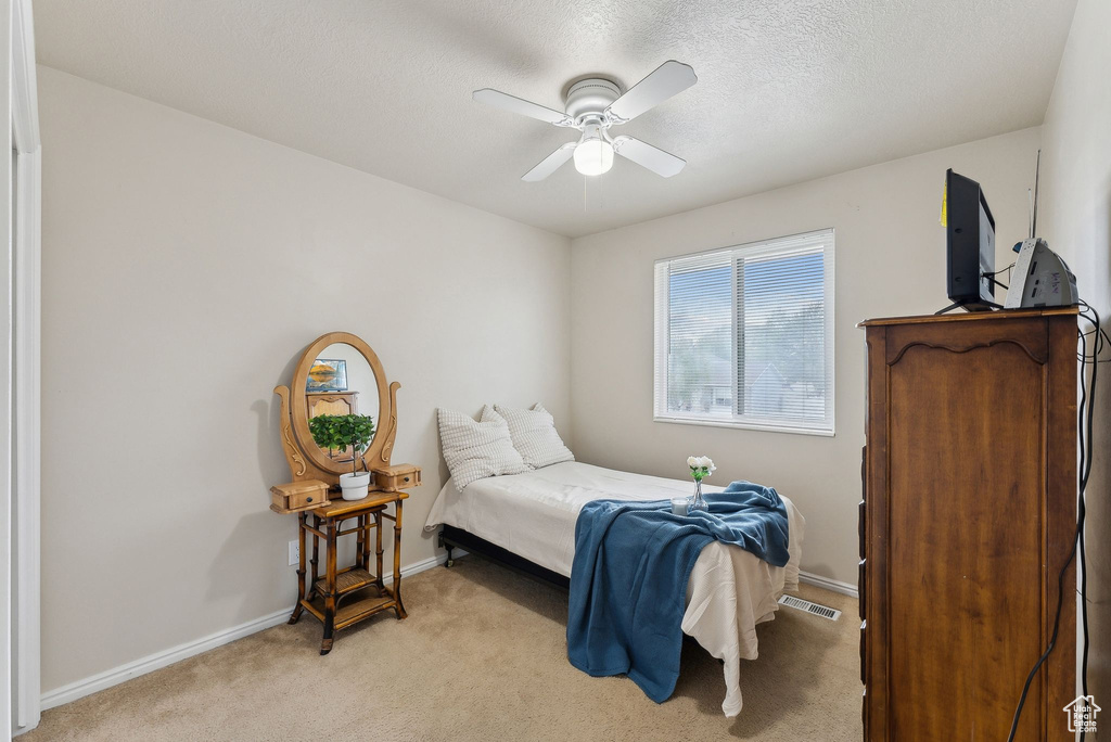 Bedroom with visible vents, light carpet, baseboards, ceiling fan, and a textured ceiling