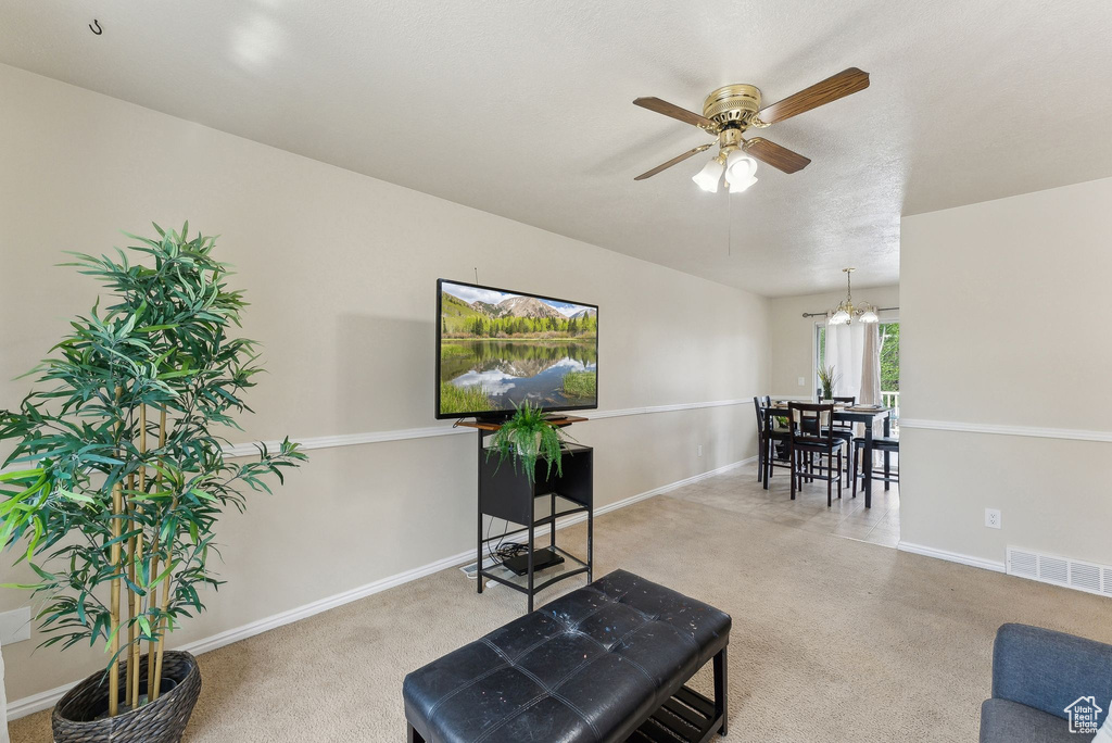 Living area with carpet floors, baseboards, visible vents, and ceiling fan with notable chandelier