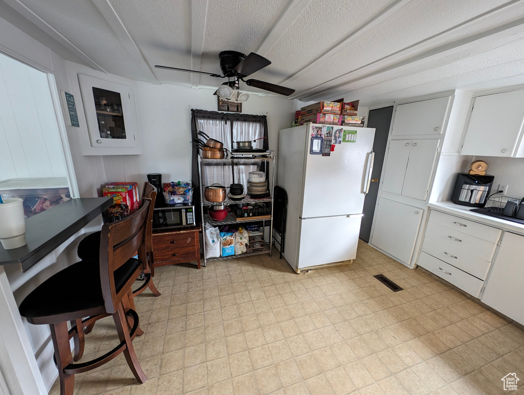 Kitchen featuring freestanding refrigerator, a ceiling fan, stainless steel microwave, and white cabinetry