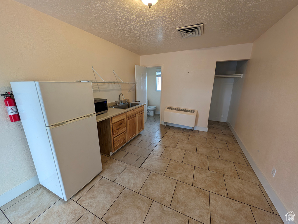 Kitchen featuring visible vents, freestanding refrigerator, a textured ceiling, stainless steel microwave, and a sink