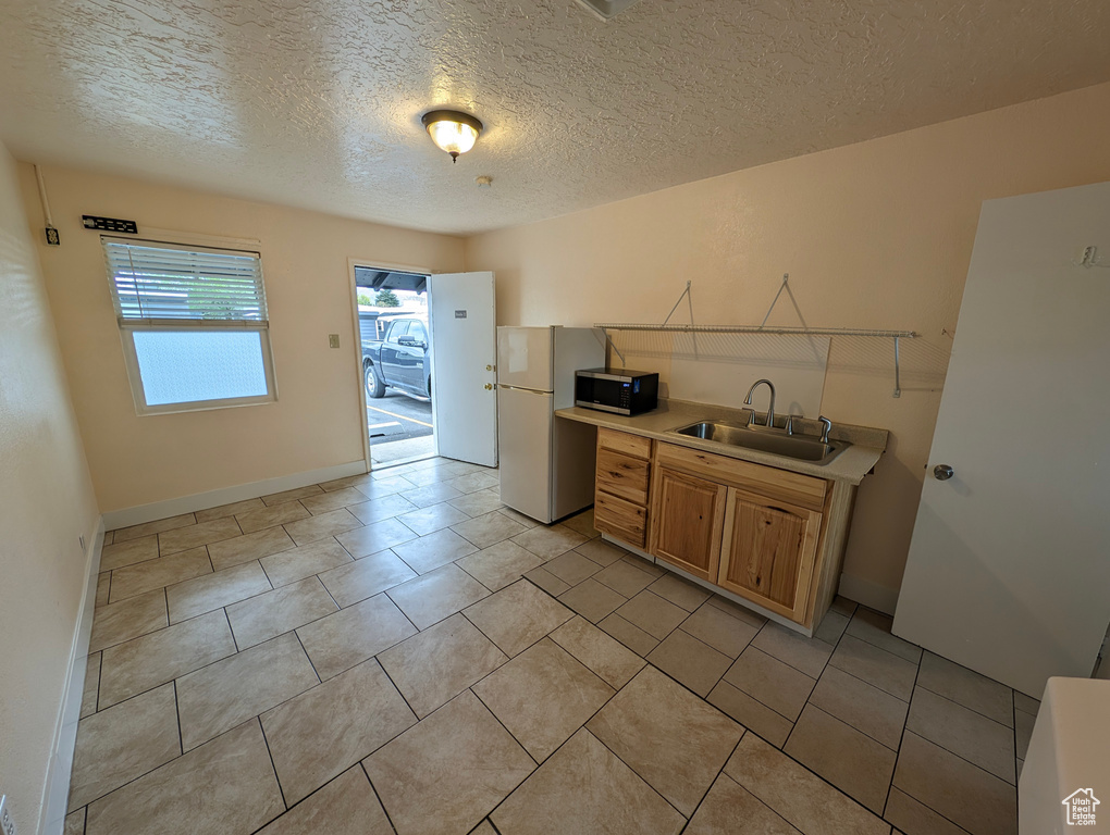 Kitchen with a textured ceiling, a sink, light countertops, freestanding refrigerator, and stainless steel microwave