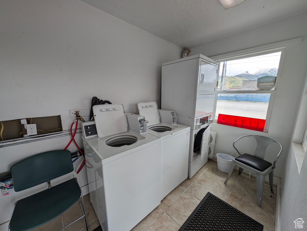 Community laundry room with light tile patterned floors, stacked washer / drying machine, and a textured ceiling