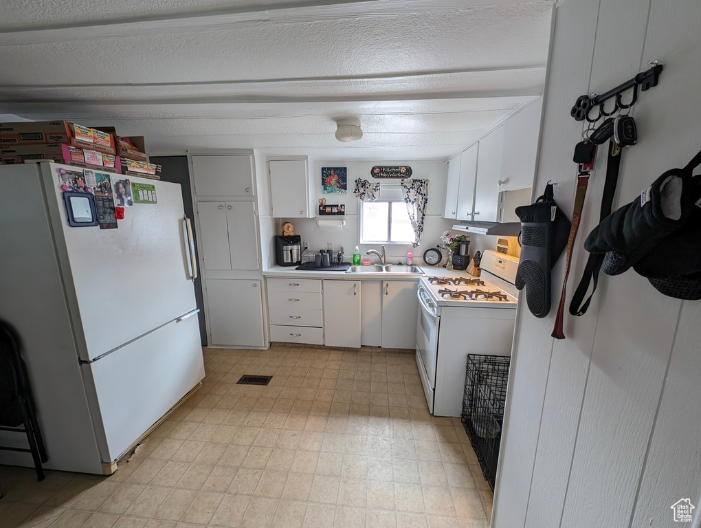 Kitchen with white cabinets, a sink, white appliances, light countertops, and light floors