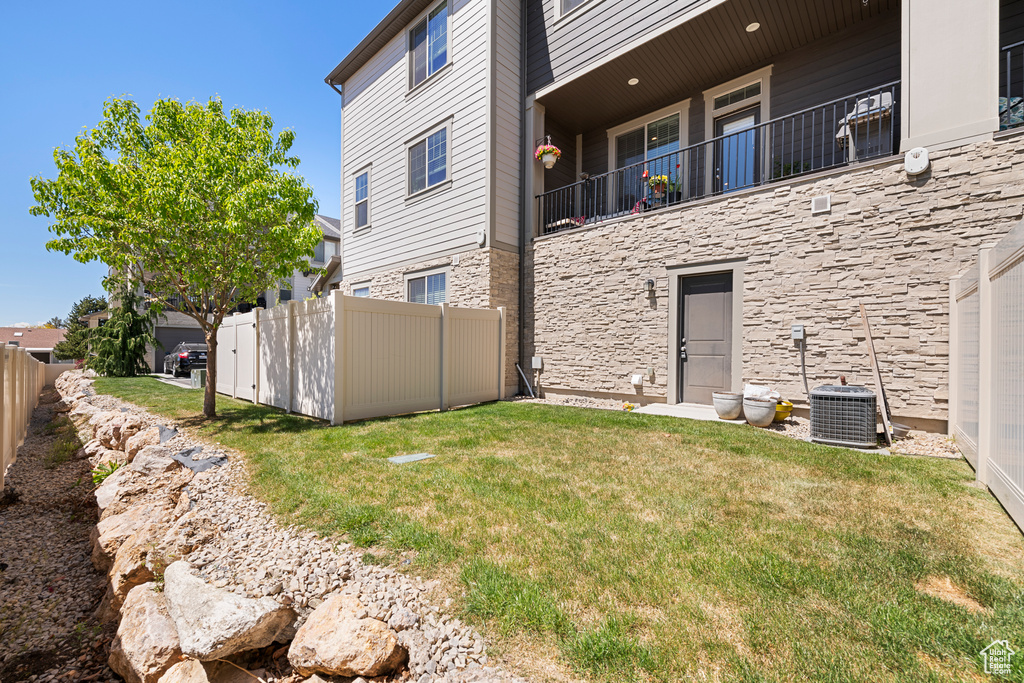 Back of property featuring a yard, fence, stone siding, and cooling unit
