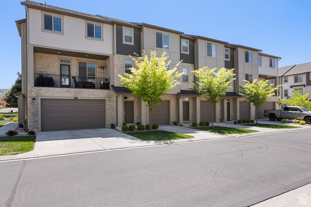Townhome / multi-family property featuring a garage, a residential view, driveway, and stone siding