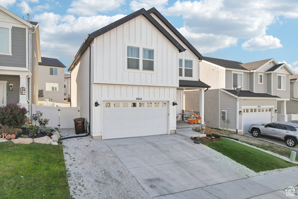 View of front facade with fence, a front lawn, a garage, board and batten siding, and driveway