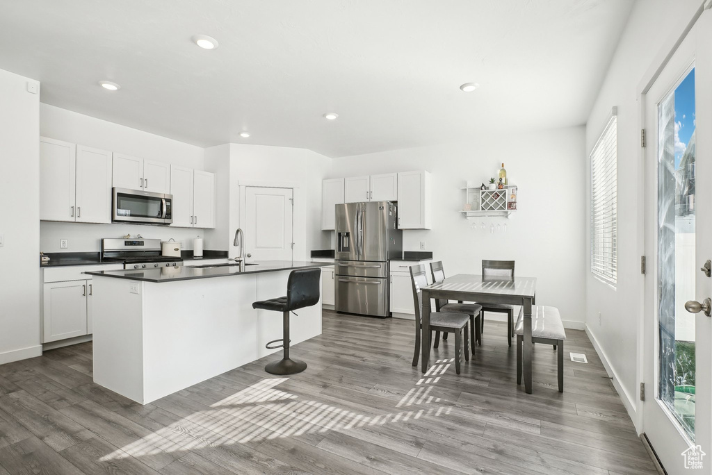 Kitchen with a kitchen breakfast bar, a kitchen island with sink, dark countertops, wood finished floors, and stainless steel appliances