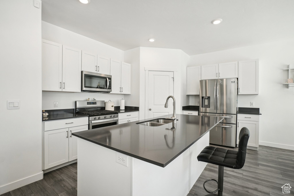Kitchen featuring a sink, appliances with stainless steel finishes, dark countertops, and dark wood-style floors