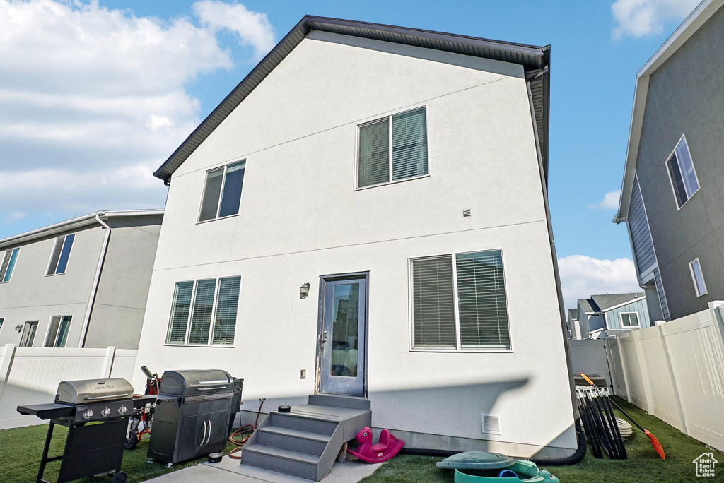 Rear view of house with stucco siding, a lawn, and fence