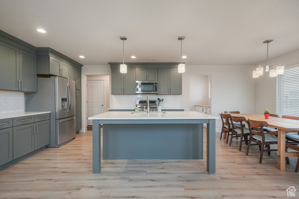 Kitchen with light countertops, light wood-style flooring, tasteful backsplash, and stainless steel appliances
