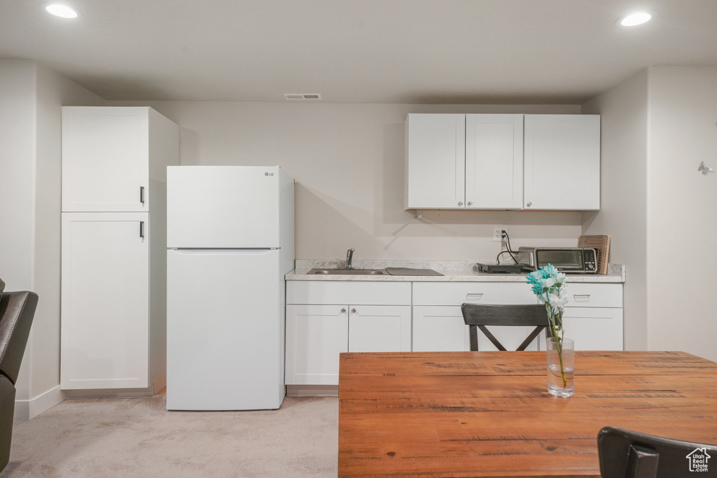 Kitchen featuring light colored carpet, a sink, white cabinets, freestanding refrigerator, and recessed lighting