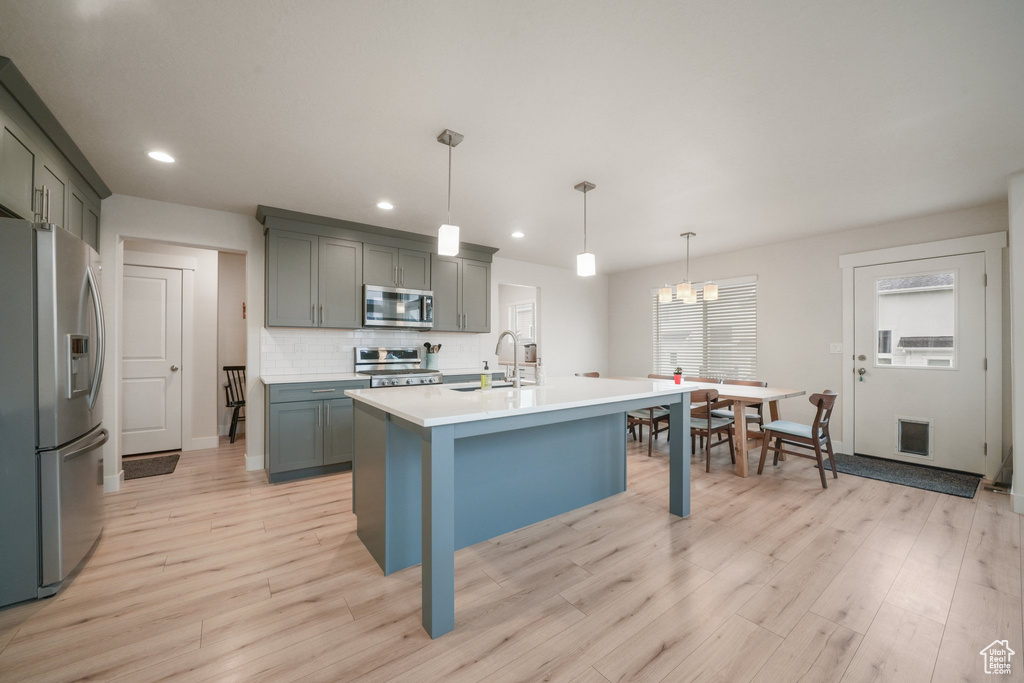 Kitchen featuring light wood-style floors, light countertops, a sink, appliances with stainless steel finishes, and backsplash