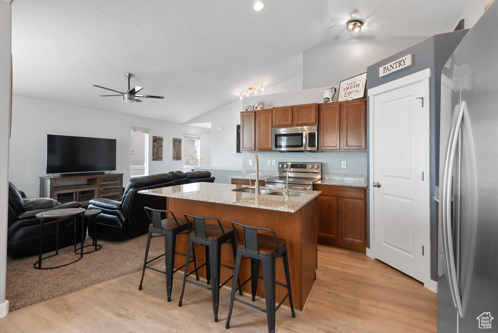 Kitchen featuring a kitchen breakfast bar, brown cabinetry, a ceiling fan, appliances with stainless steel finishes, and vaulted ceiling