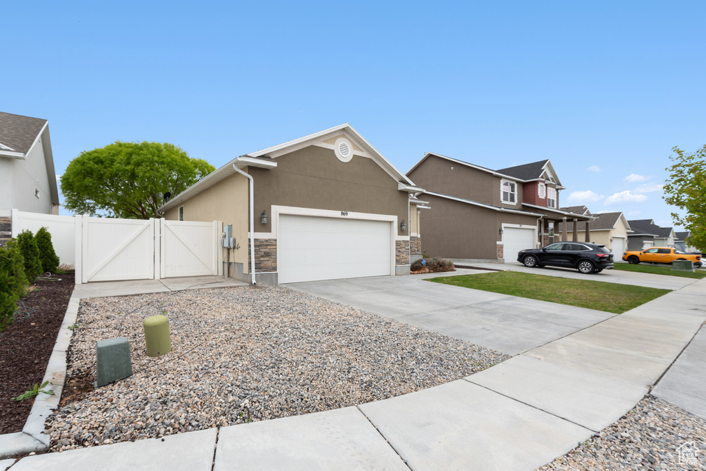 View of front of home with stone siding, stucco siding, a gate, an attached garage, and driveway