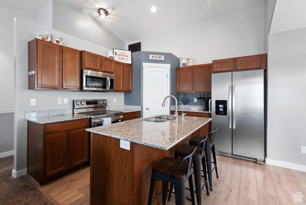 Kitchen with light stone counters, a sink, appliances with stainless steel finishes, and a kitchen breakfast bar