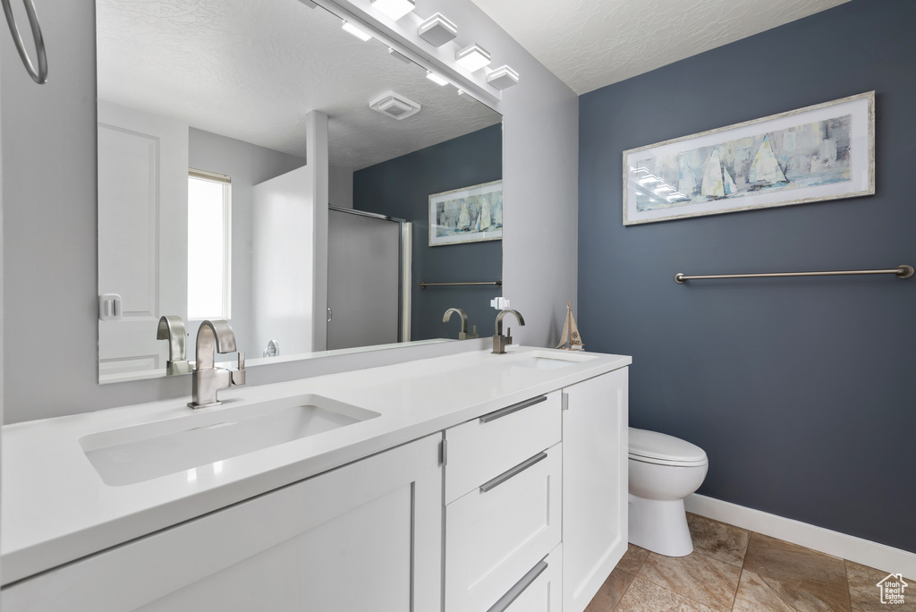 Bathroom featuring double vanity, a sink, a stall shower, and toilet