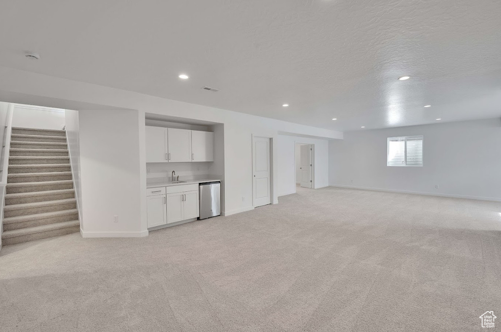 Basement with stairs, light carpet, indoor wet bar, baseboards, and a sink