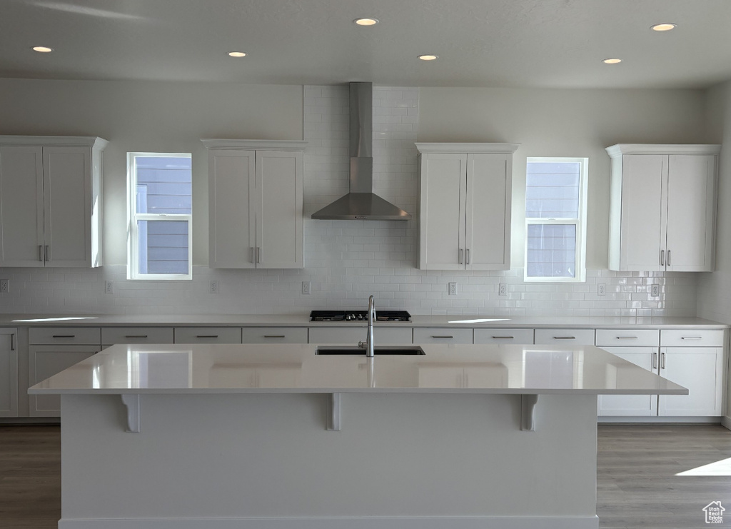 Kitchen with wall chimney range hood, tasteful backsplash, a kitchen bar, and light wood-type flooring