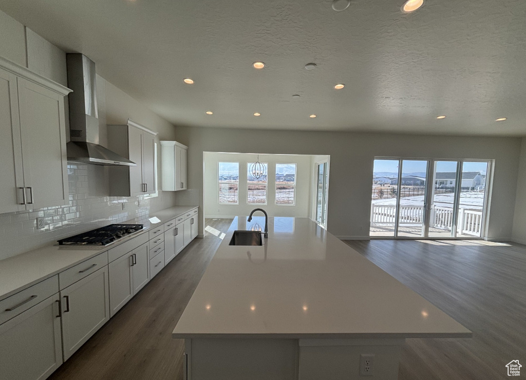 Kitchen with wall chimney range hood, stainless steel gas cooktop, a wealth of natural light, and dark wood-type flooring