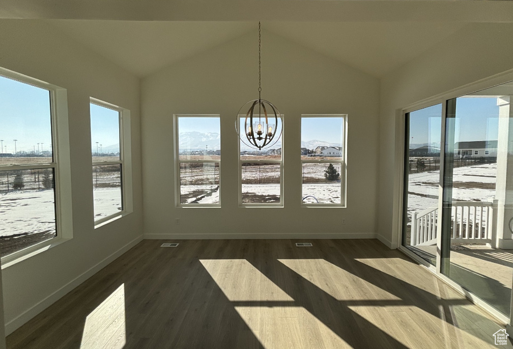Unfurnished sunroom featuring plenty of natural light, wood finished floors, a chandelier, and vaulted ceiling
