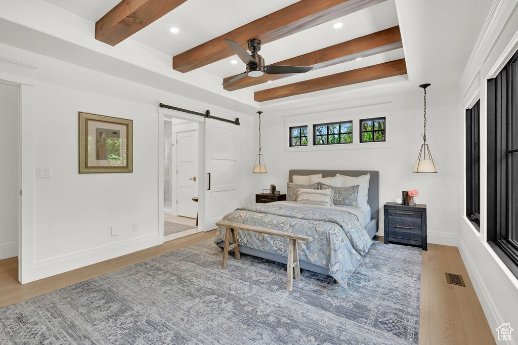 Bedroom with visible vents, wood finished floors, beamed ceiling, baseboards, and a barn door