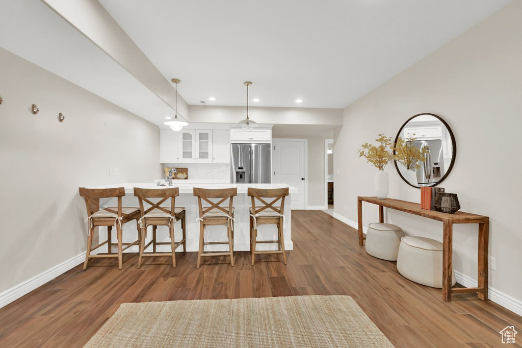 Kitchen with stainless steel fridge, a peninsula, baseboards, white cabinetry, and glass insert cabinets