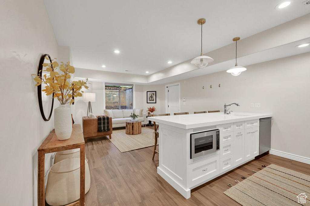 Kitchen with a peninsula, light wood-type flooring, light countertops, white cabinetry, and stainless steel appliances