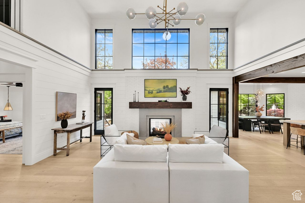 Living room with a high ceiling, a notable chandelier, plenty of natural light, and light wood-style floors