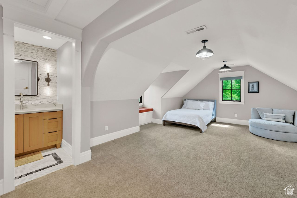 Bedroom featuring visible vents, lofted ceiling, baseboards, light colored carpet, and ensuite bath