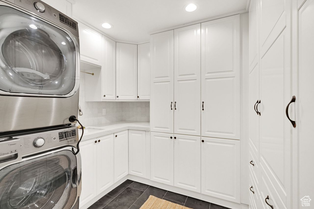 Clothes washing area with dark tile patterned flooring, cabinet space, recessed lighting, and stacked washer / dryer