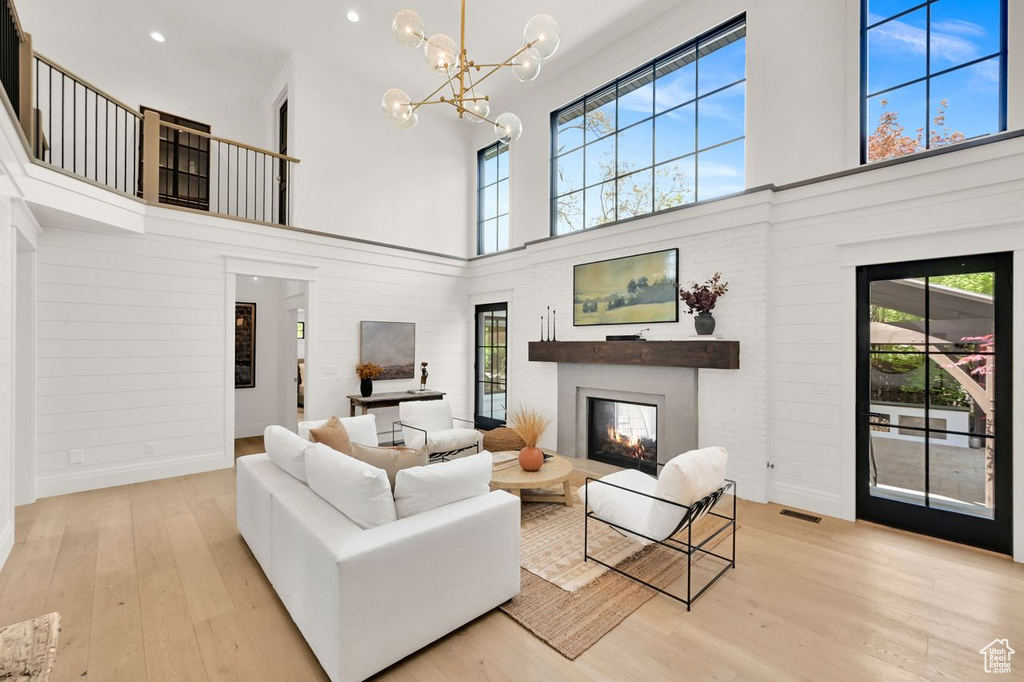 Living area featuring a notable chandelier, a glass covered fireplace, wood finished floors, a towering ceiling, and visible vents