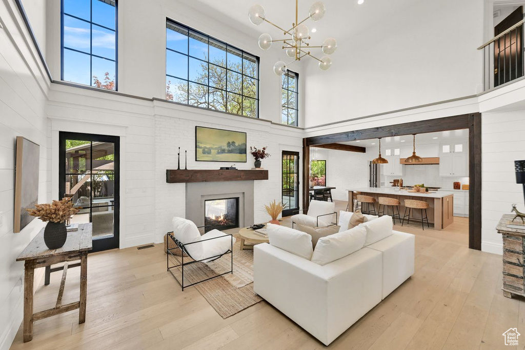 Living room with light wood-style floors, a glass covered fireplace, a high ceiling, and an inviting chandelier