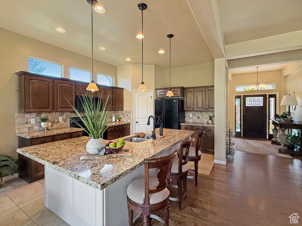 Kitchen featuring decorative backsplash, a breakfast bar, a center island with sink, a sink, and black fridge