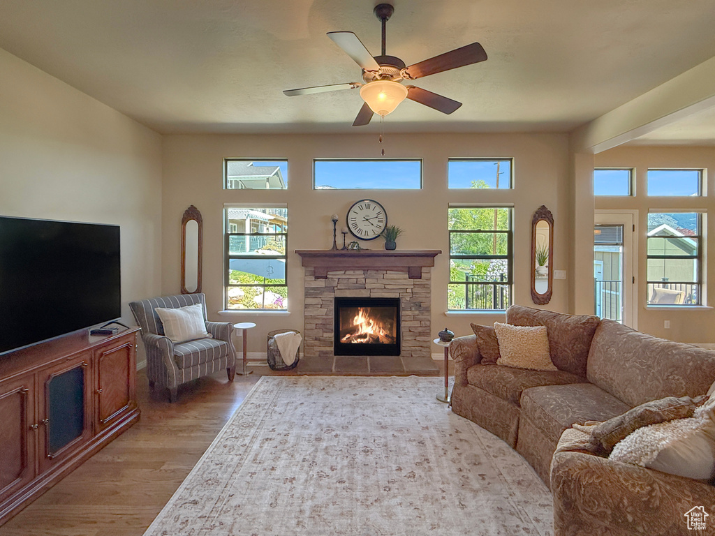 Living room with a ceiling fan, a stone fireplace, a healthy amount of sunlight, and light wood-style floors